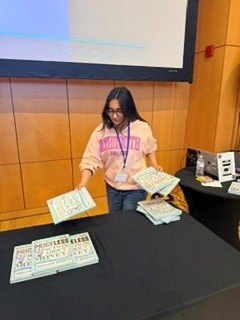 Sophia arranging stacks of financial-literacy books on a table in an auditorium.